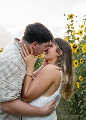 A romantic couple shares tender kisses in front of a blooming sunflower field during golden hour.