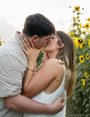 A romantic couple shares an intimate kiss among blooming sunflowers at sunset.
