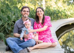 A family sits together on a wooden dock surrounded by greenery on a sunny day.