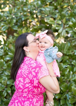 A woman in a bright pink floral dress shares joyful moments with a baby in a garden setting.