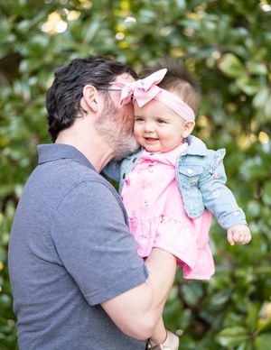 A tender moment captured outdoors with a baby wearing pink and denim against a green leafy background.