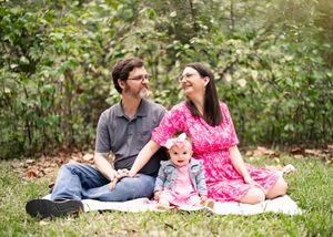 Happy family sitting together on blanket in garden wearing pink and grey casual clothes while laughing.