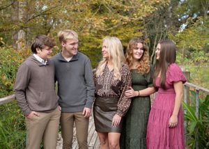 A group of young people stand together outdoors in casual fall attire against an autumn foliage backdrop.
