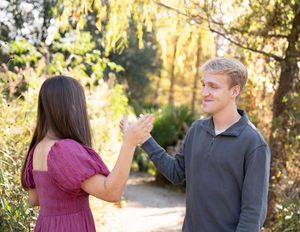 A couple shares a playful moment together on a sunlit path surrounded by autumn foliage.