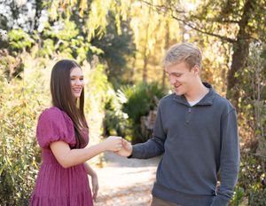 Couple in a romantic autumn photoshoot outdoors with golden sunlight filtering through trees in the background.