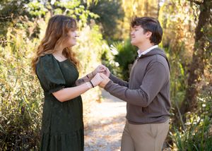 A romantic proposal moment captured in a sunlit forest setting with autumn foliage in the background.