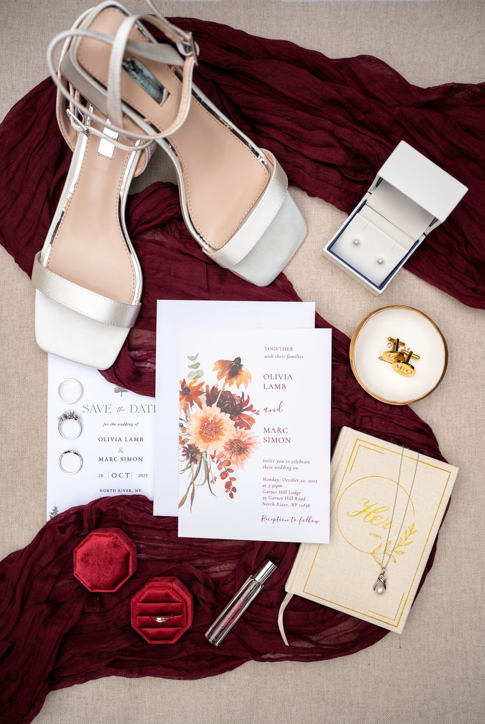 Burgundy velvet fabric with white wedding invitations and blush pink bridal shoes arranged on neutral linen background.