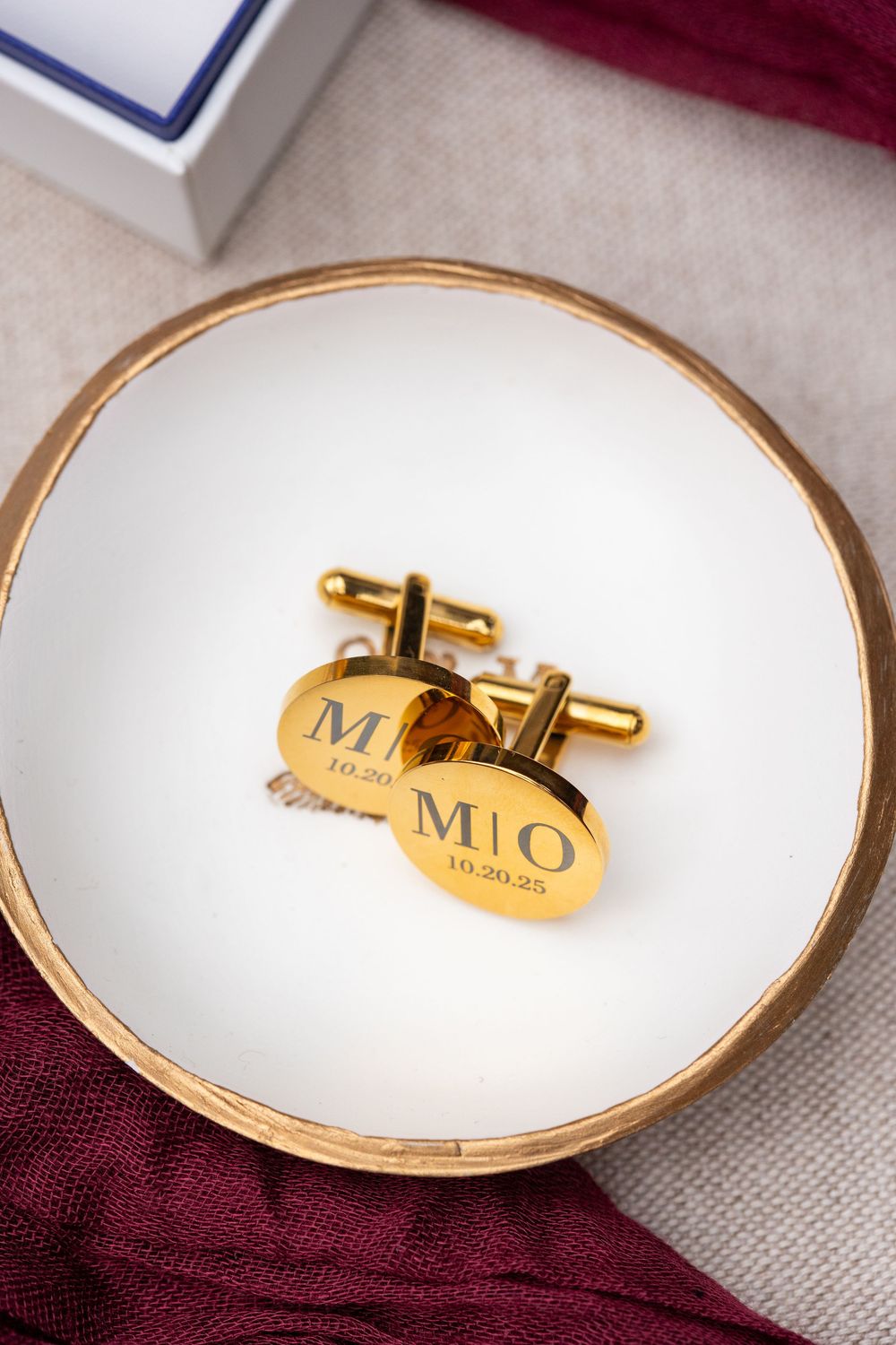 Gold monogram cufflinks displayed on white porcelain plates with gold trim for a wedding.