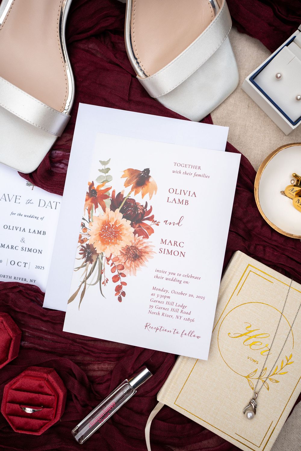 Wedding invitation suite featuring floral designs in soft peach and burgundy tones laid out on velvet fabric.