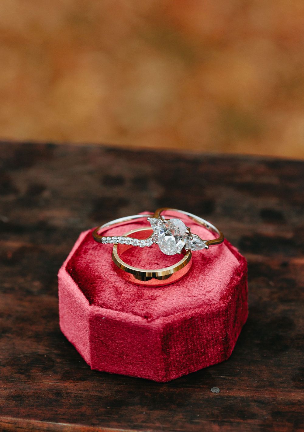 Wedding rings displayed on a red velvet octagonal ring box on dark wood surface.