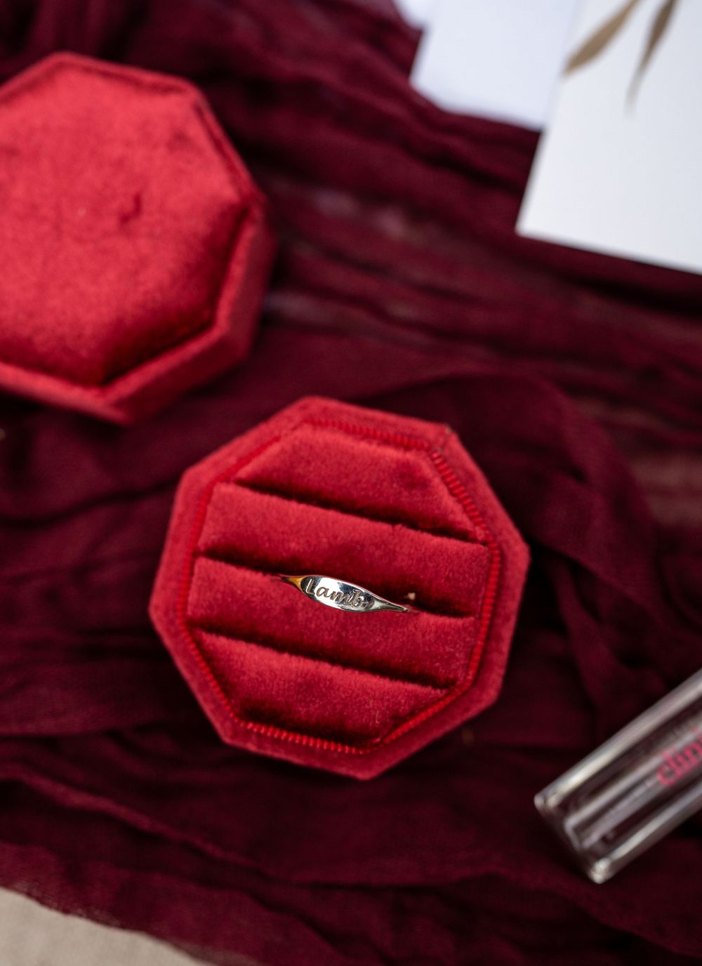 Diamond engagement ring displayed in red velvet octagonal ring box on burgundy fabric.
