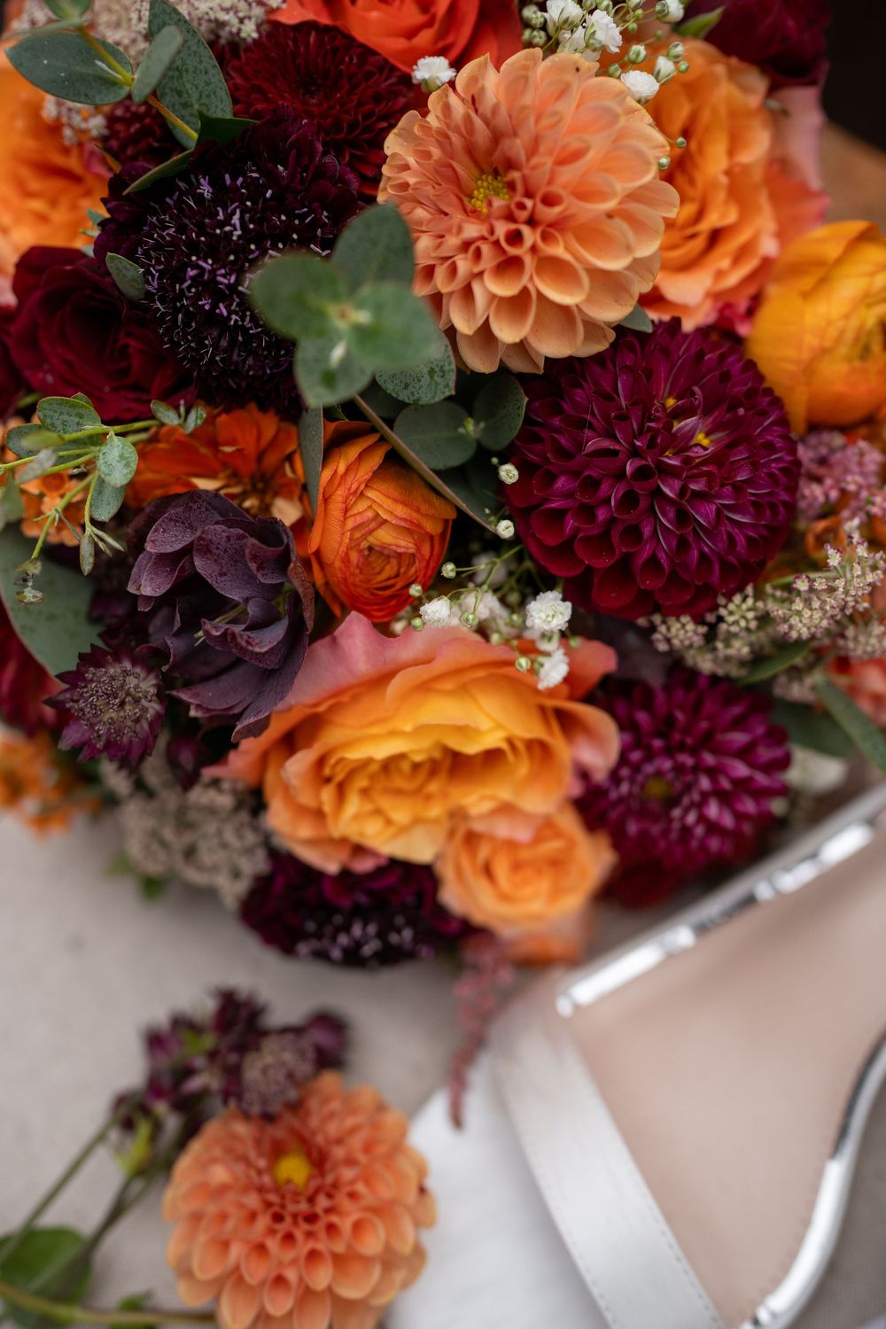 Vibrant autumn wedding bouquet with orange roses, burgundy dahlias, and delicate baby's breath flowers.