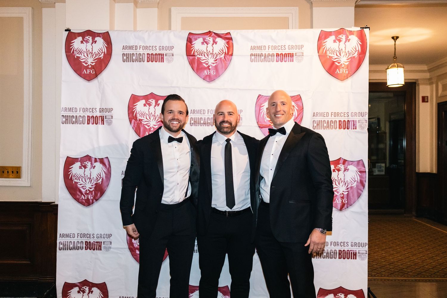 Three gentlemen in tuxedos standing together at a formal event.