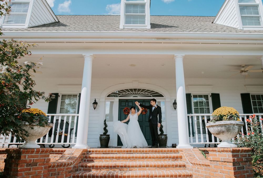 A panoramic view of a classic white colonial house with brick steps and pillared front porch on a sunny day.