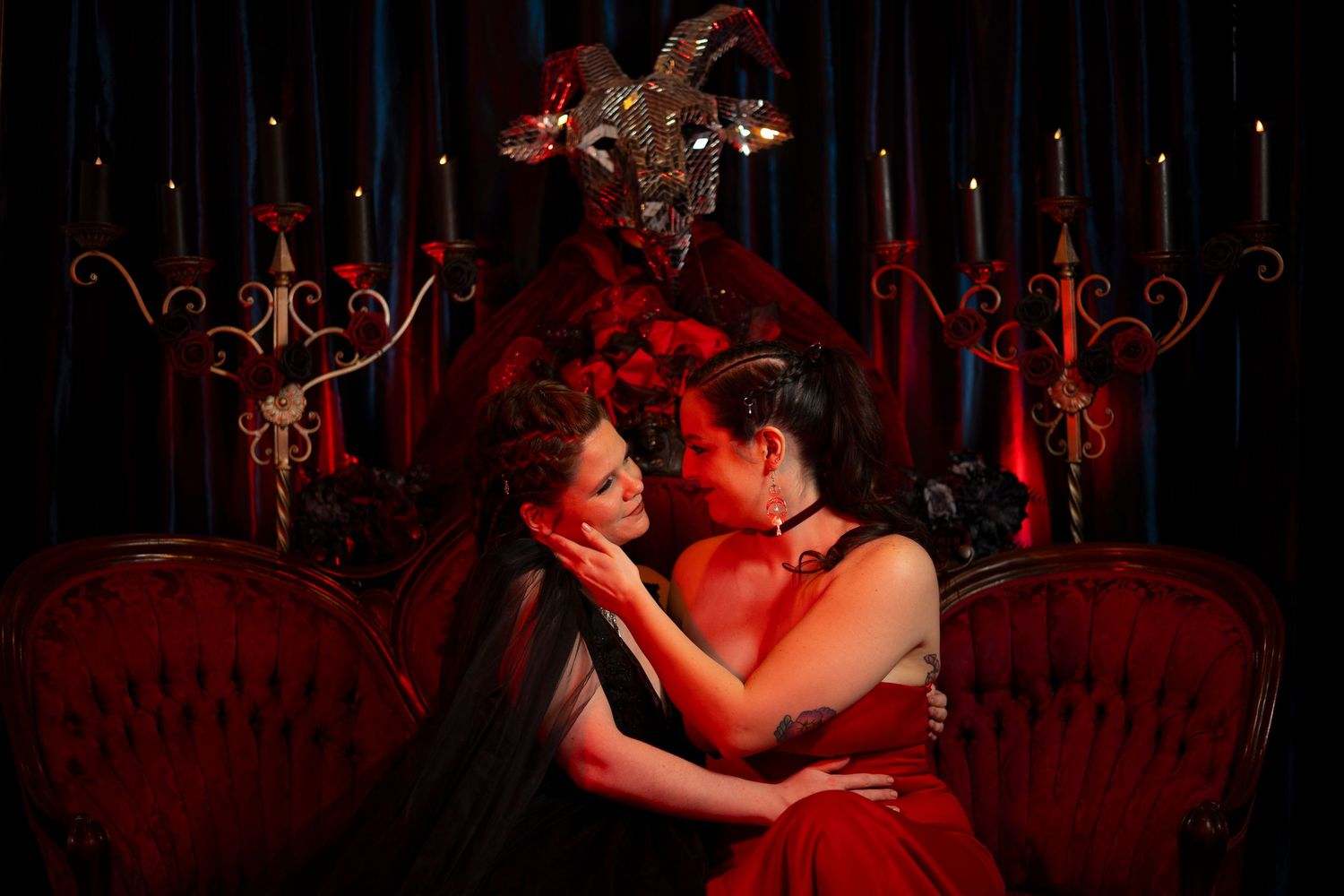 A couple in formal attire dances together in a dimly lit ballroom with red lighting and ornate decor.