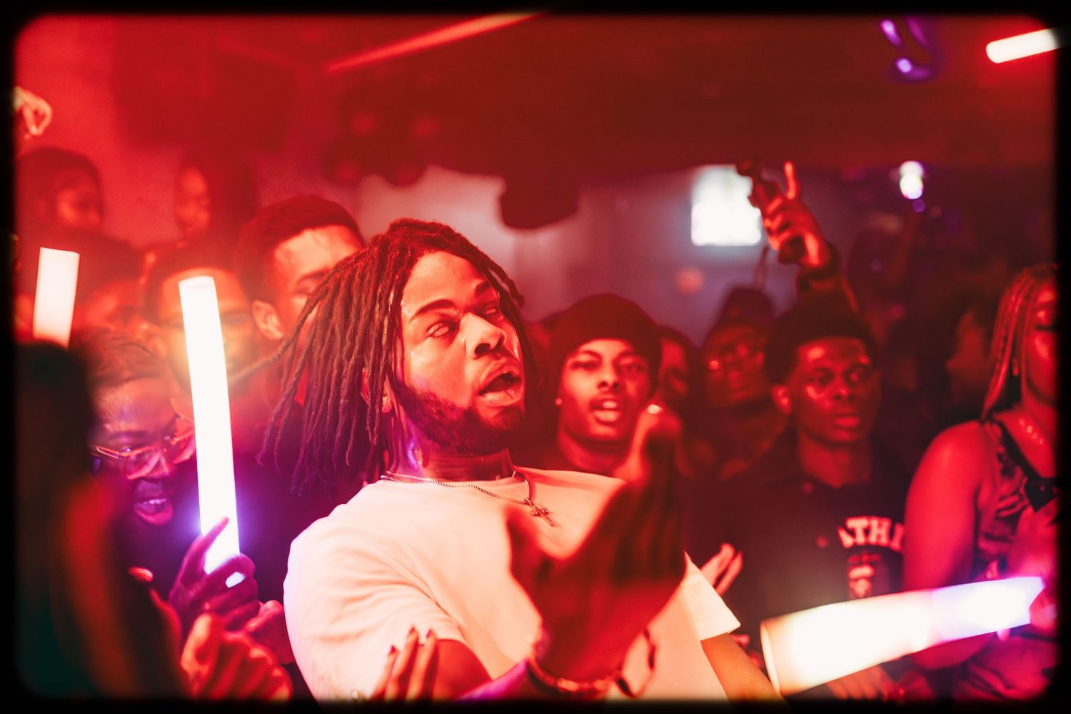 Crowd of people dancing at a nightclub under red lighting with glowsticks and party atmosphere.