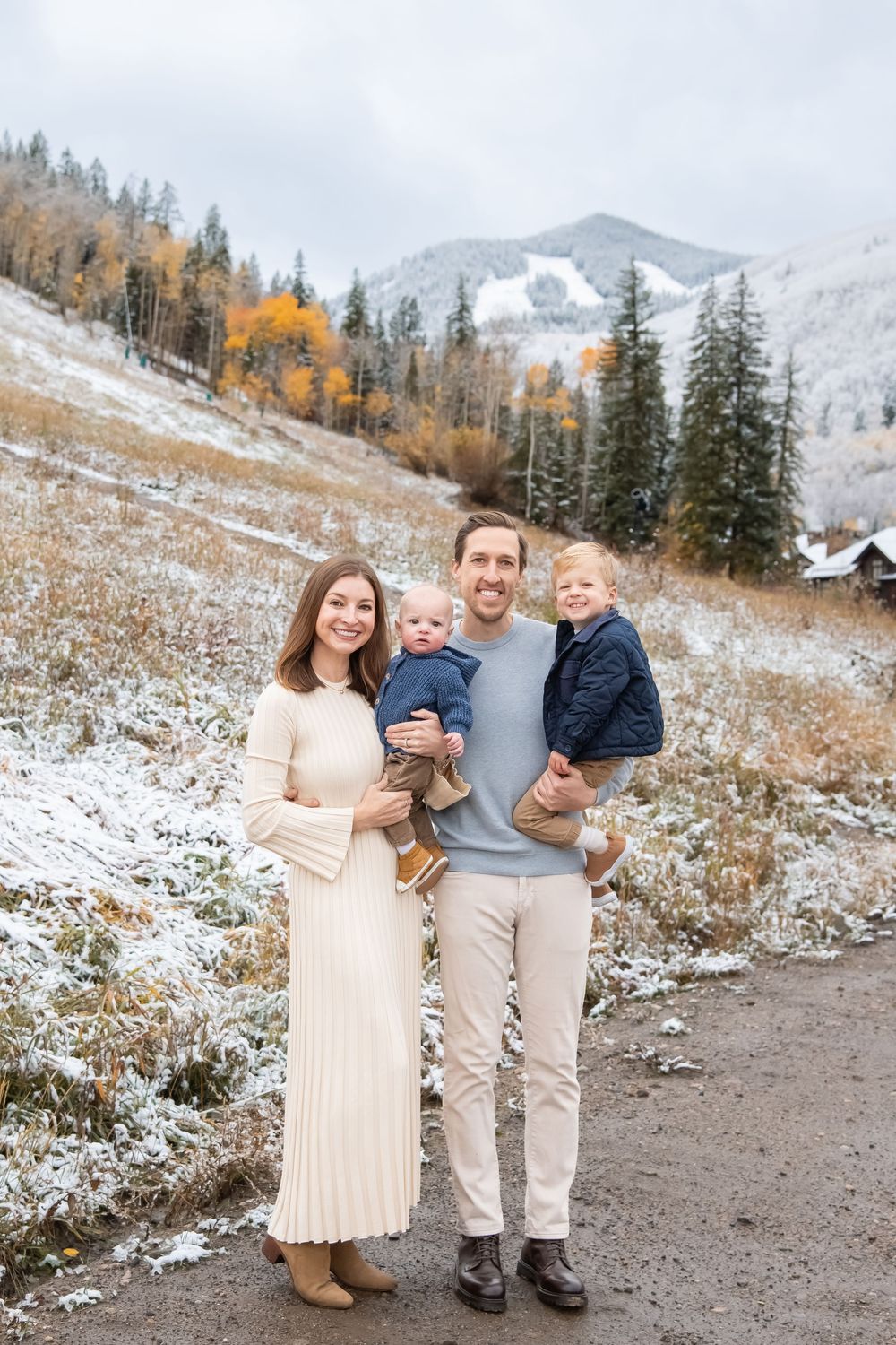Snow-covered mountain landscape with autumn trees and people in light-colored clothing standing on a dirt path.