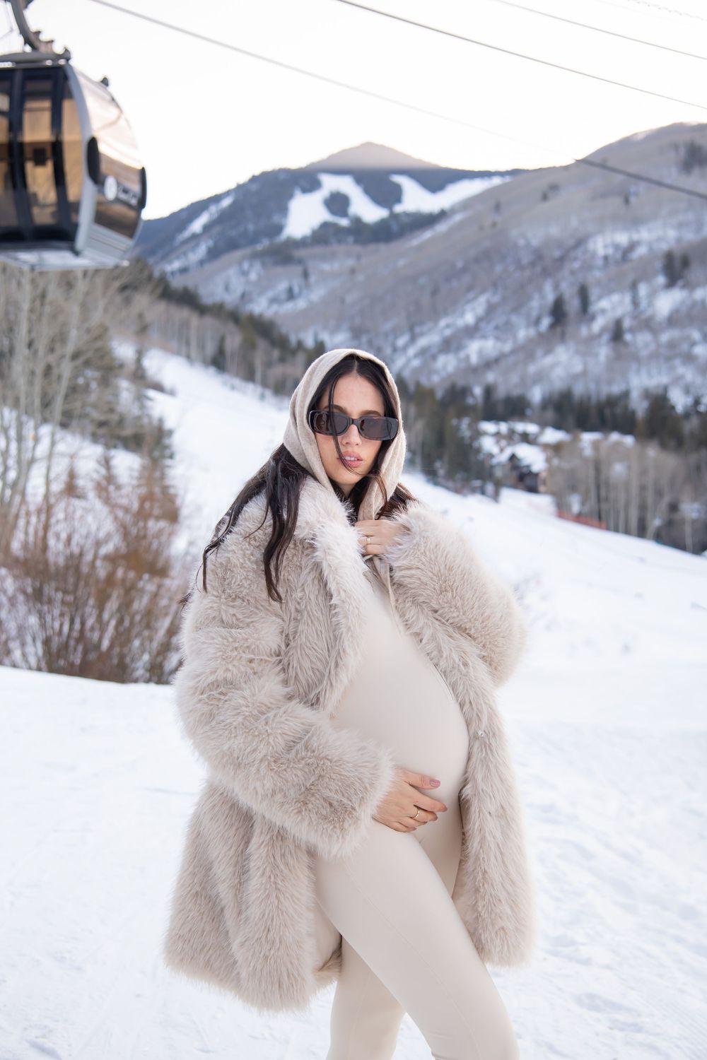 Winter fashion photoshoot featuring cream colored fur coat and matching outfit against snowy mountain backdrop.