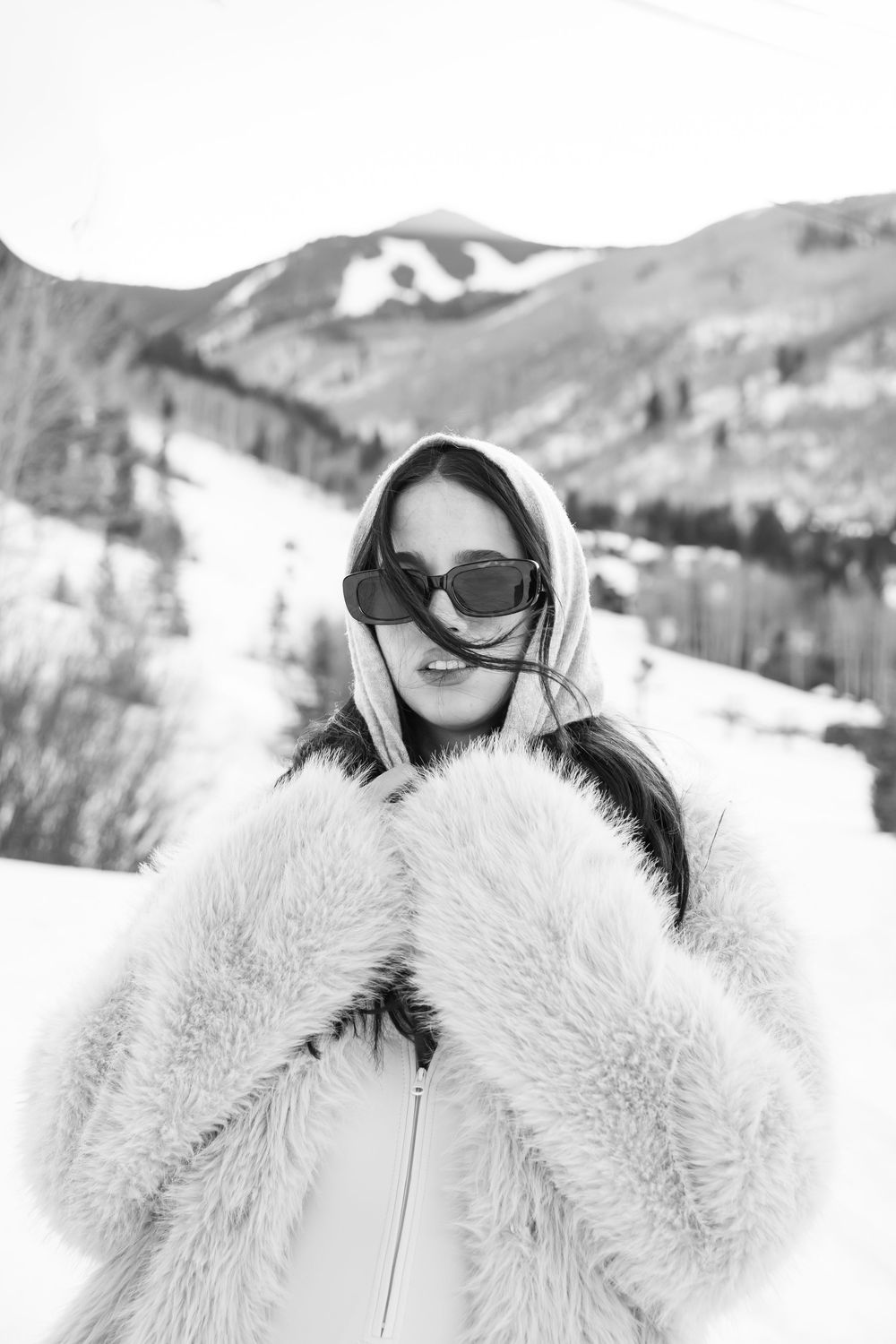 Person wearing white winter coat and sunglasses smiling in snowy mountain landscape.