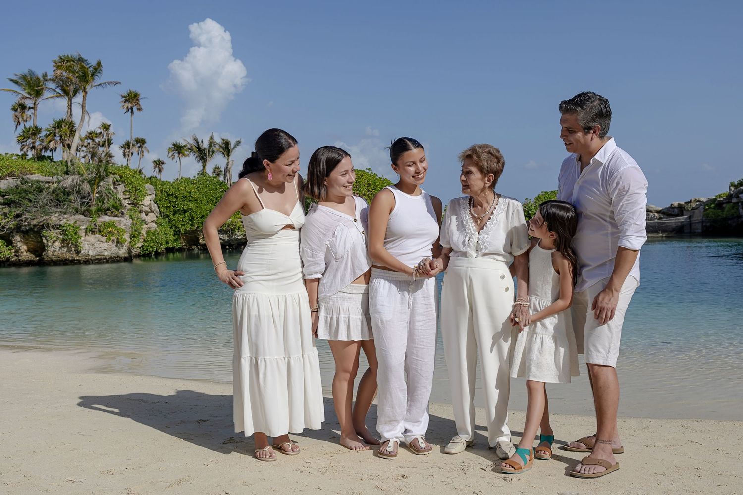 Family gathered on the beach, sharing a joyful moment with their grandmother at Hotel Xcaret Mexico.