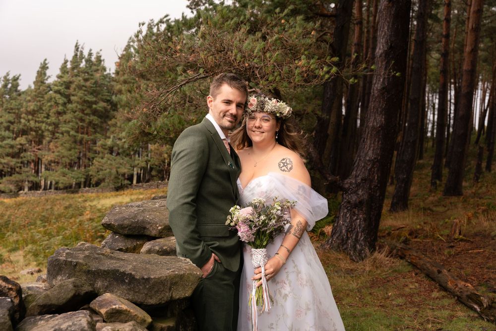A couple shares an intimate moment in a forest setting with tall pine trees and natural light filtering through.