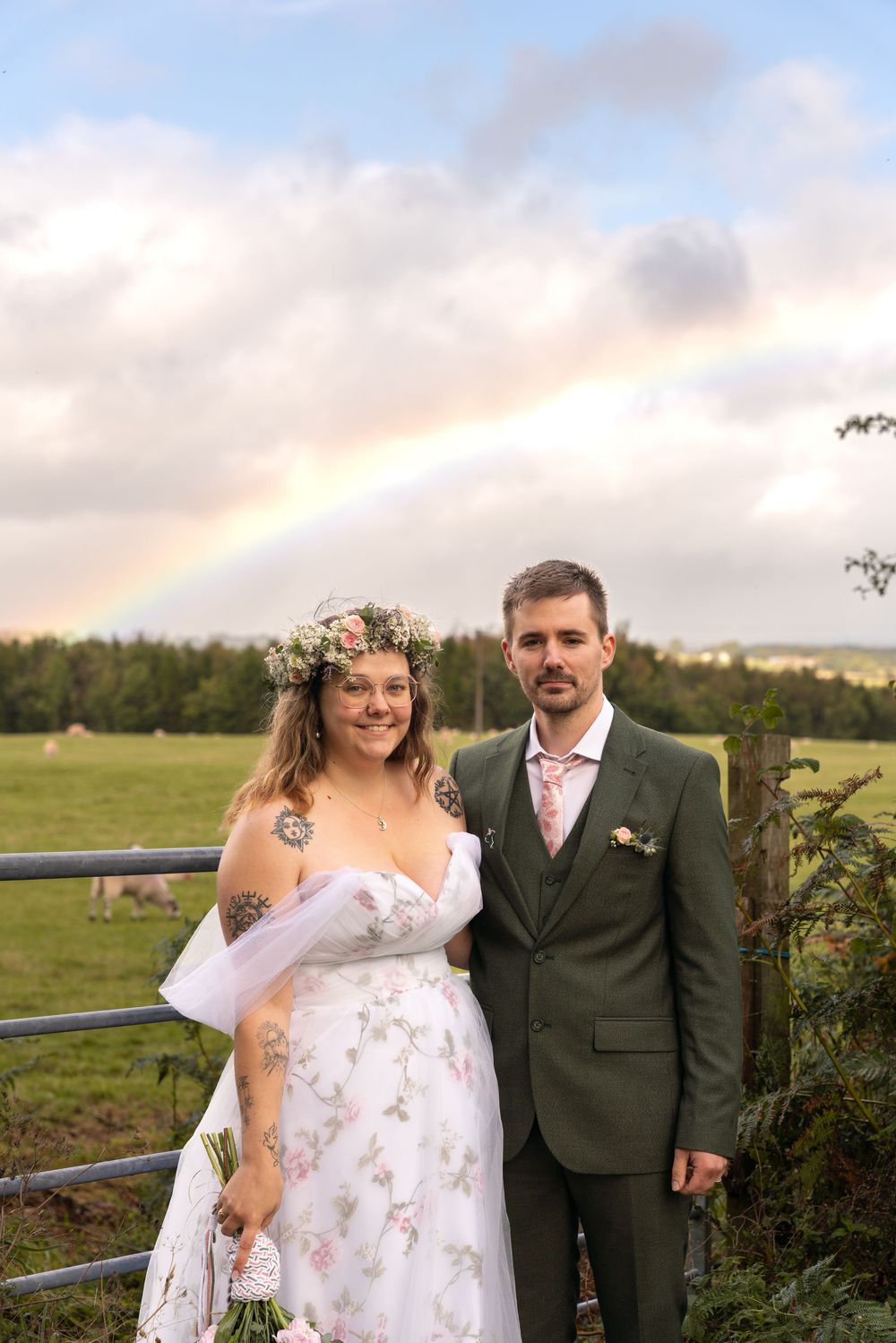 Newlywed couple poses together in pastoral field with cloudy sky during sunset wedding photography session.