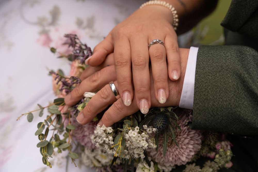 Close-up shot of hands holding a rustic wedding bouquet with white and purple flowers against a light fabric background.