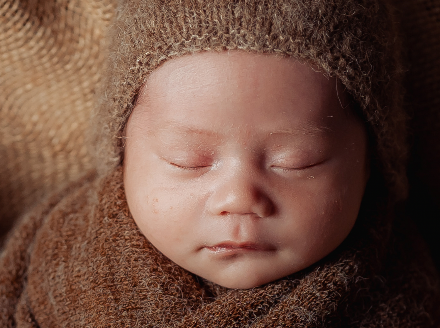Artistic newborn photo series showing peaceful sleeping baby in brown wrapping.