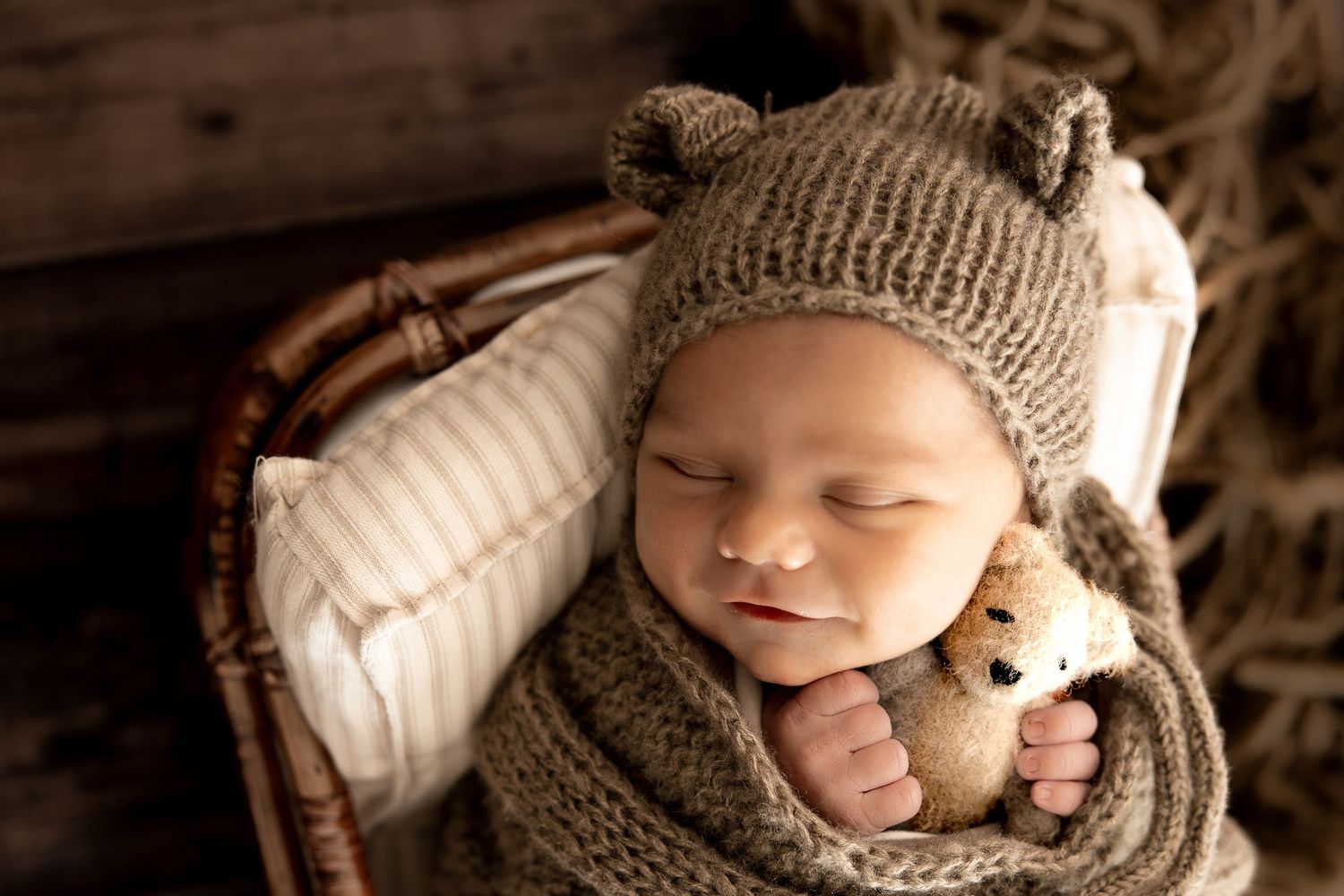 Wrapped newborn baby smiling while holding a small teddy bear plushie, photographed during a newborn session in Central Indiana