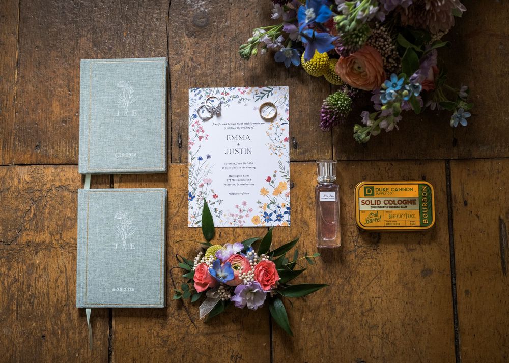 Flat lay of Emma and Justin wedding stationery, rings, cologne, and colorful floral bouquet.