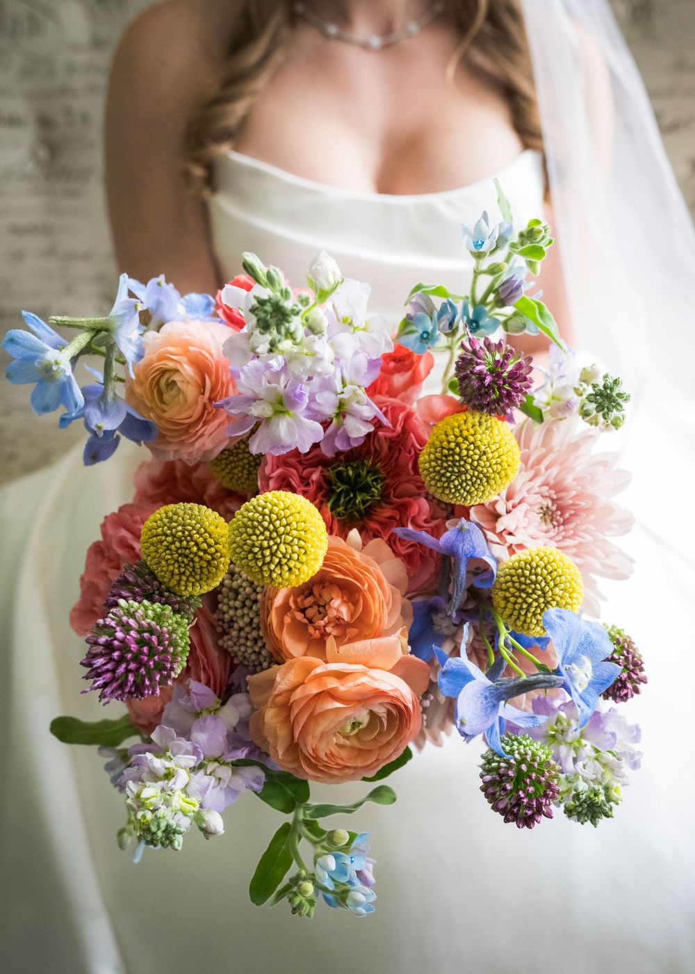 Bride holding vibrant colorful wedding bouquet with ranunculus, dahlias, and blue delphinium.