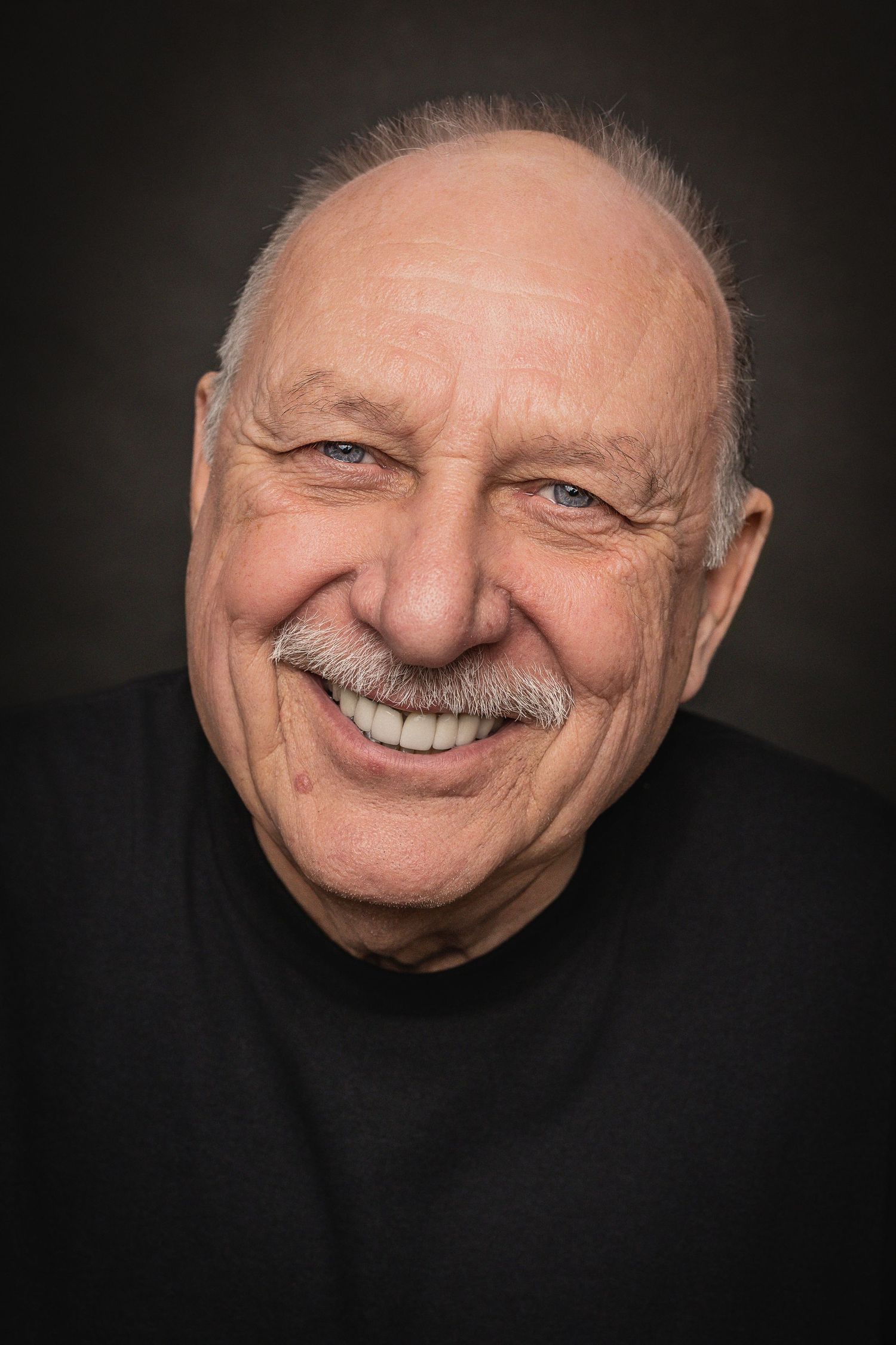 Close-up portraits of a smiling elderly person with white mustache against dark background showing different angles.