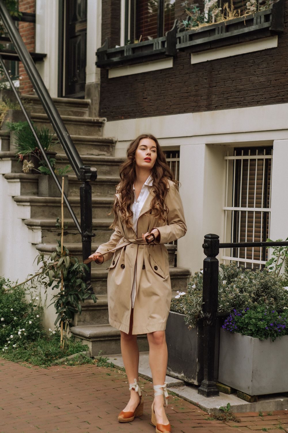 Fashion photo series showing a beige trench coat and white dress outfit on a cobblestone street in Amsterdam.