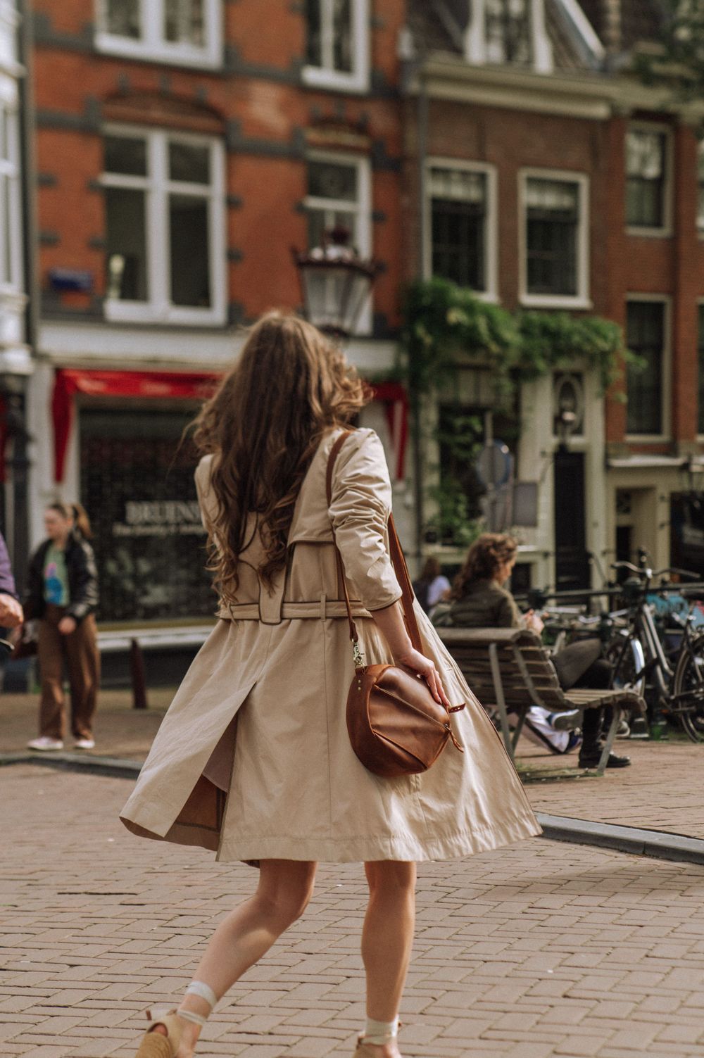 Street style photos capturing movement in a beige coat and white dress on historic Amsterdam streets.