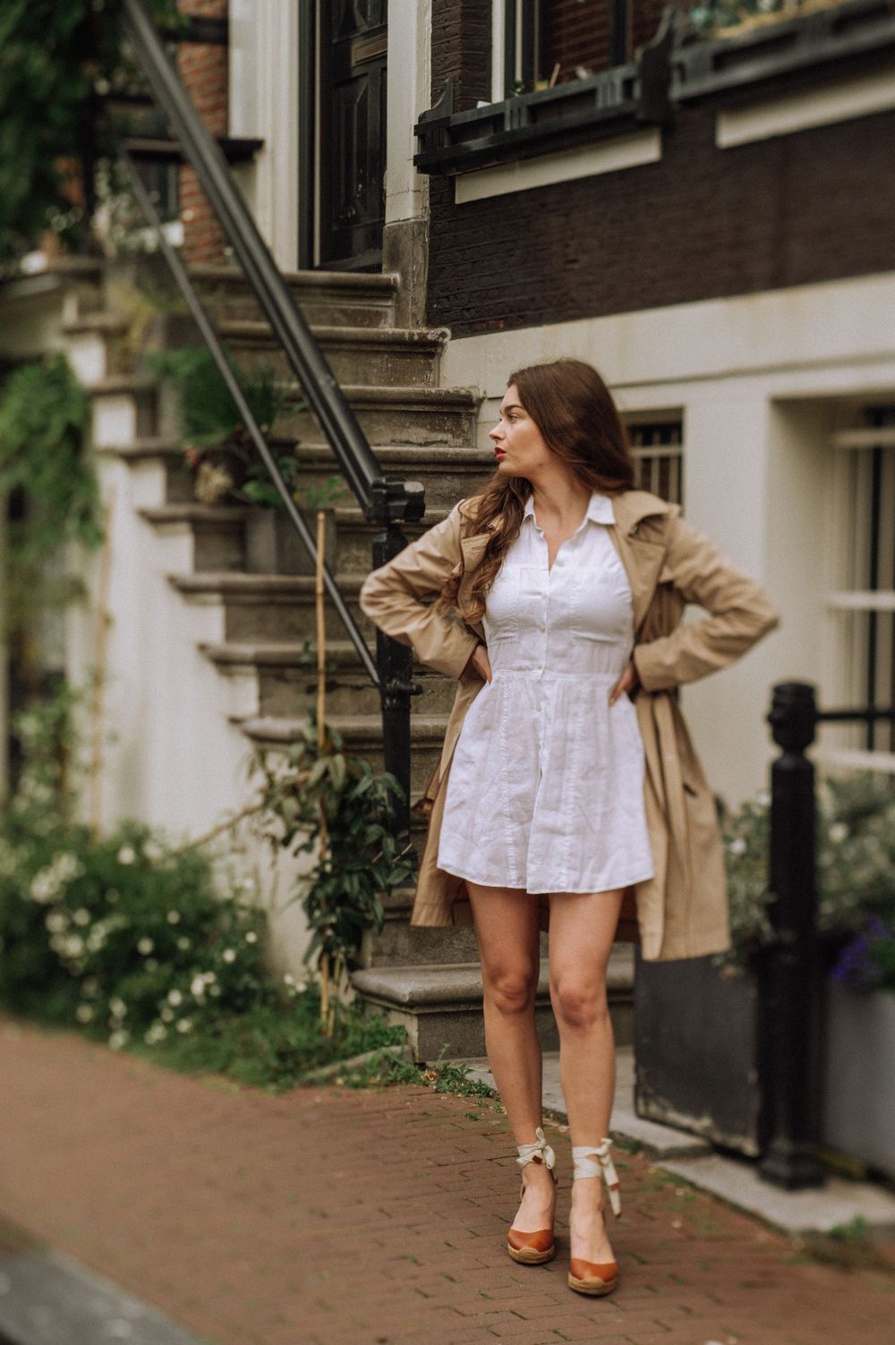 Fashion editorial featuring a classic trench coat and white dress combination against urban architecture.