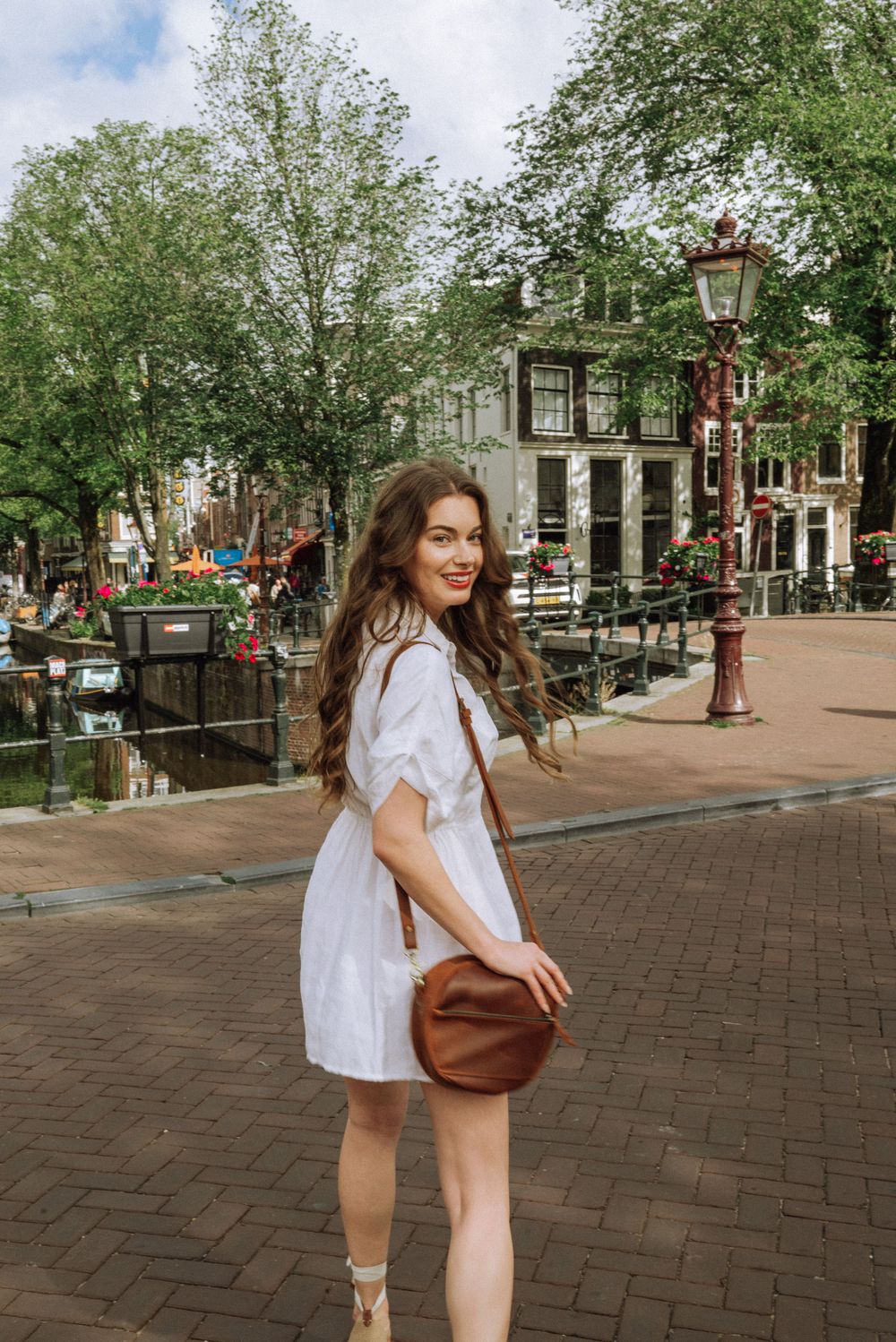 Person in white dress walking along brick-paved street with historic Dutch buildings and trees.