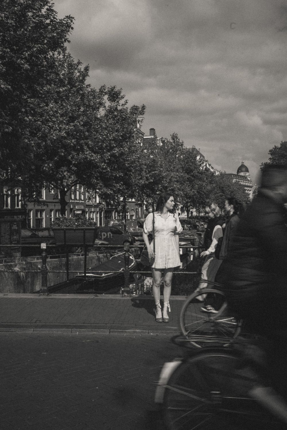 Motion blur sequence of people walking along a tree-lined canal in Amsterdam on a cloudy day.