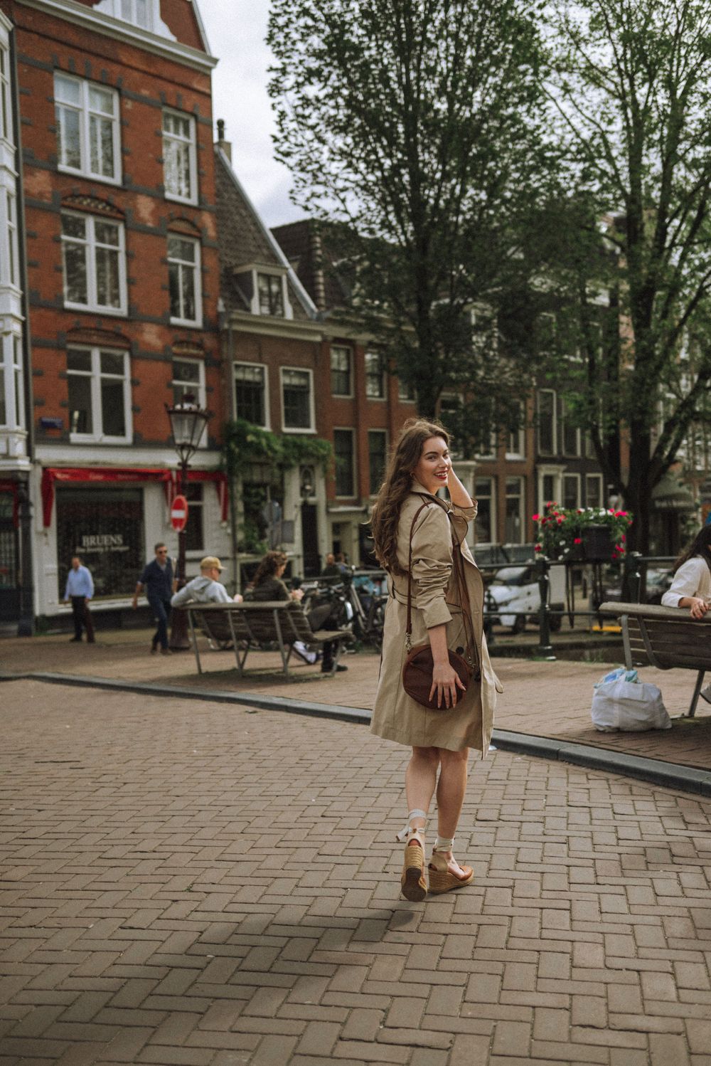 Person in beige coat walking across brick plaza with historic Dutch buildings in background.