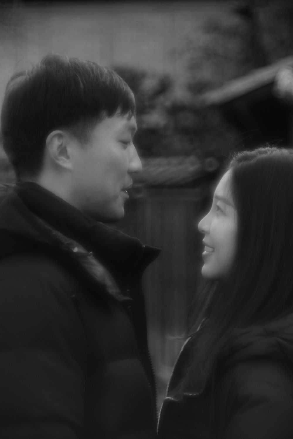 Black and white portrait of smiling Asian couple gazing at each other lovingly outdoors.