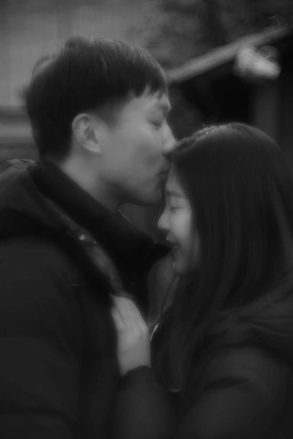 Blurred black and white artistic photo of Asian couple sharing a tender kiss while embracing.