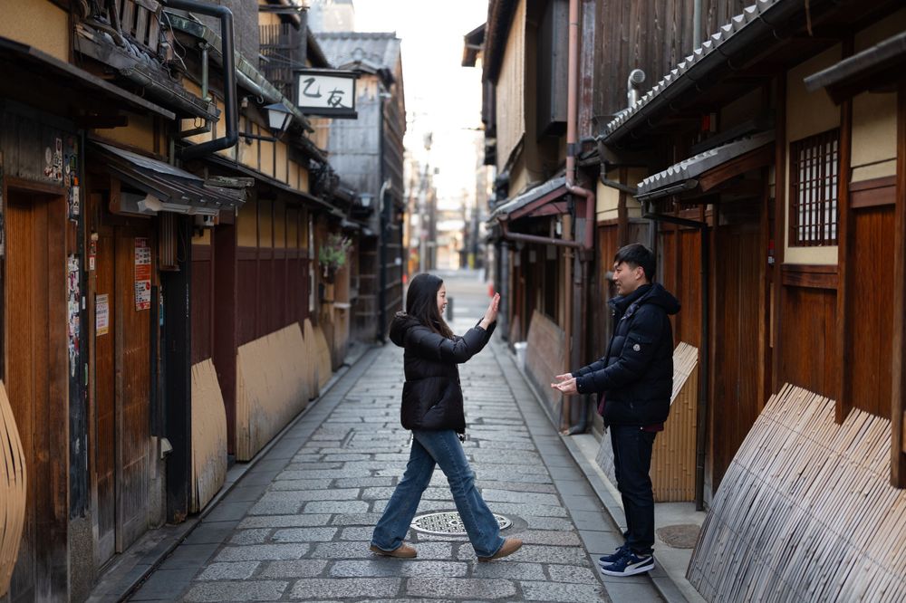 Couple playfully interact on a historic cobblestone street flanked by traditional Japanese machiya townhouses in Kyoto.