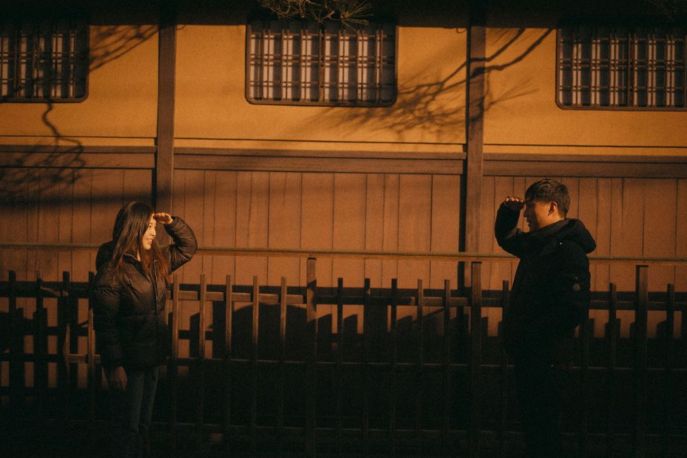 Couple playfully photographing each other at night in front of a traditional Japanese building.