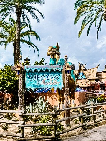 Colorful tropical theme park entrance with palm trees, wooden fence, and mystic lagoon sign in teal and turquoise colors.