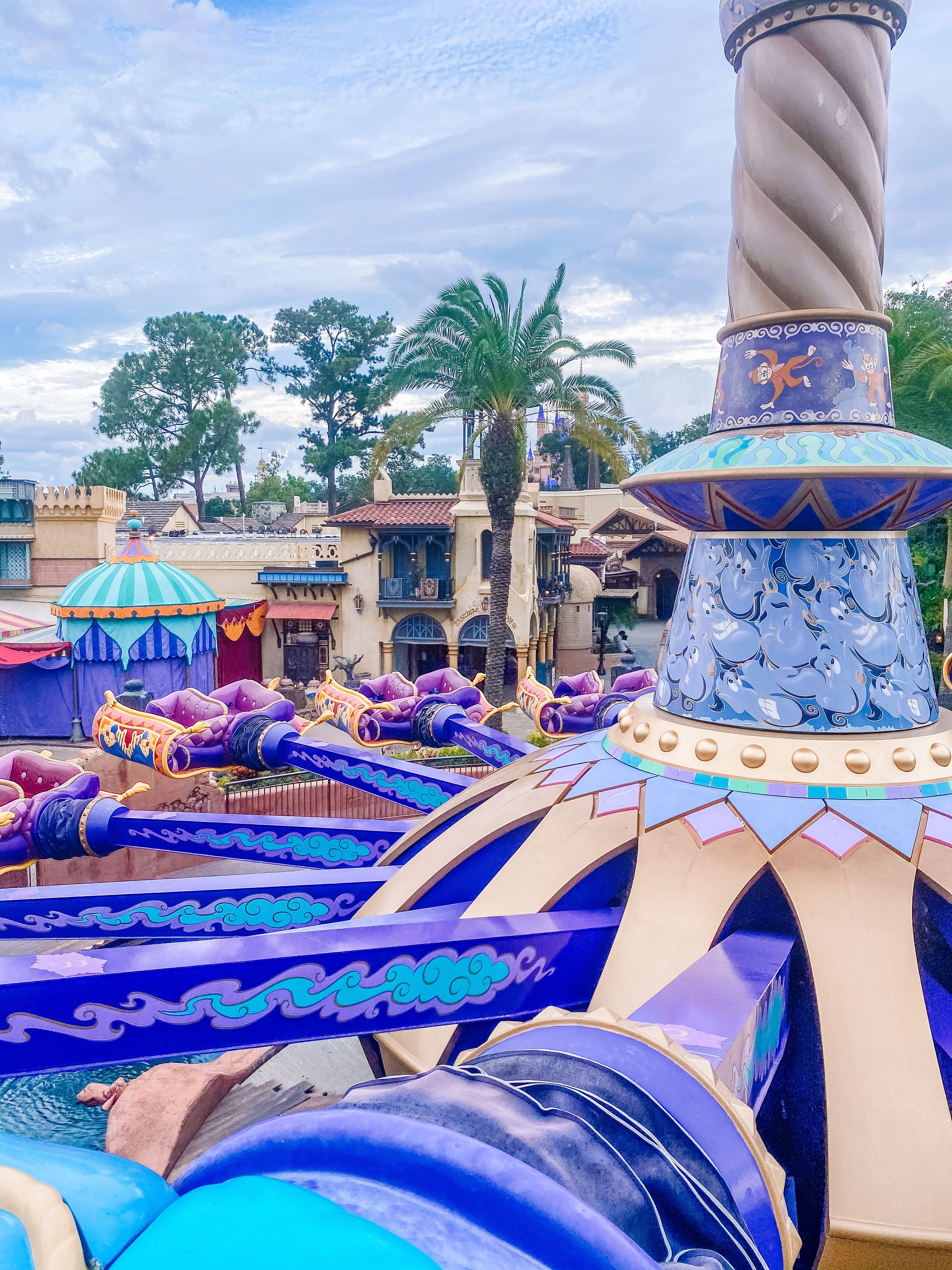 Colorful carpets with oriental patterns flow through a theme park attraction featuring decorative arches and palm trees.