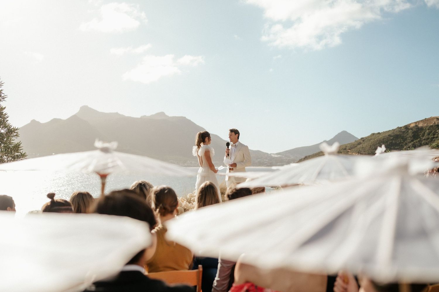 A wedding ceremony takes place on a scenic overlook with mountain views and blue skies in the background.