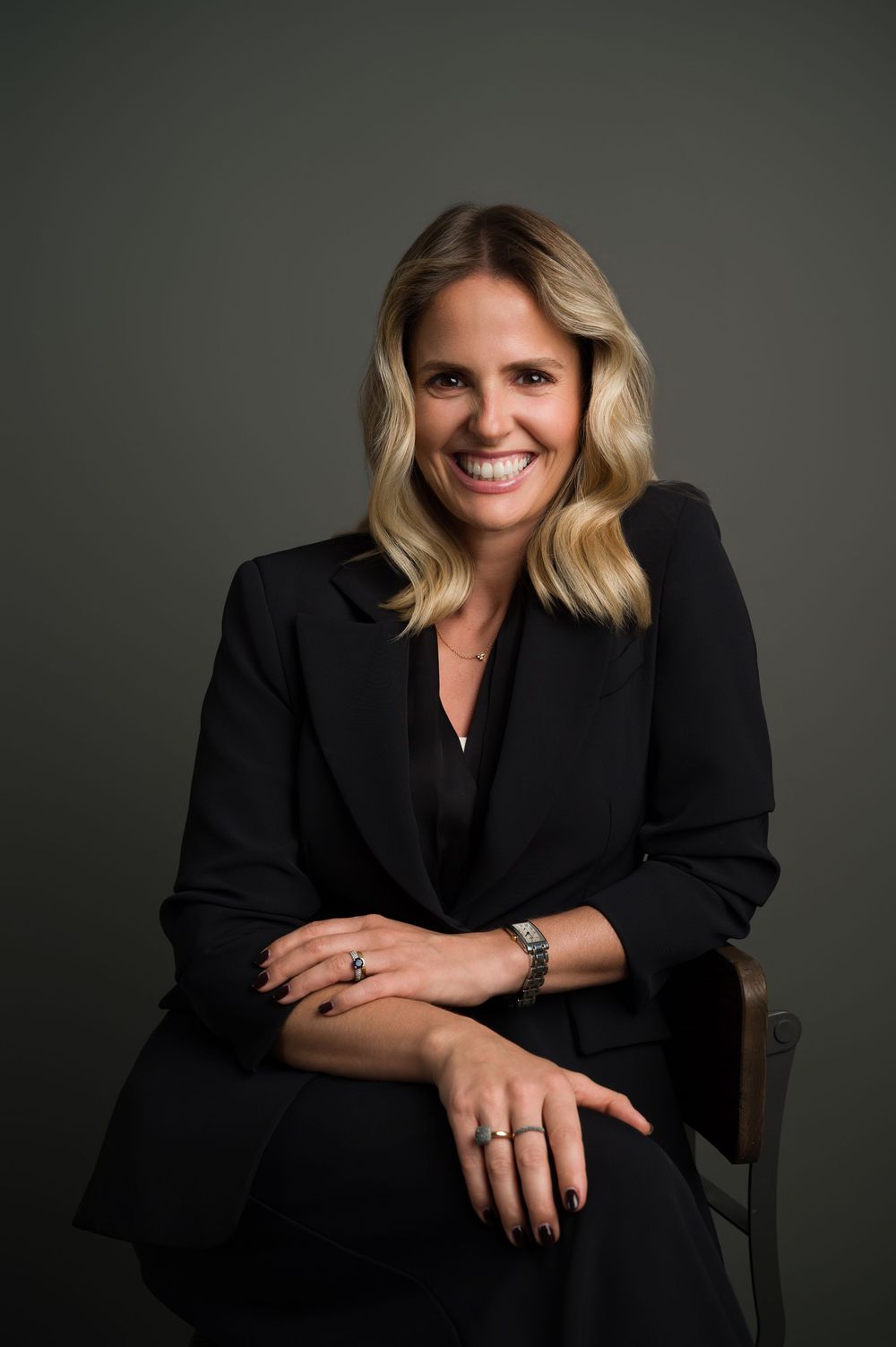 Confident blonde woman in black blazer smiling, professional corporate portrait studio photo.