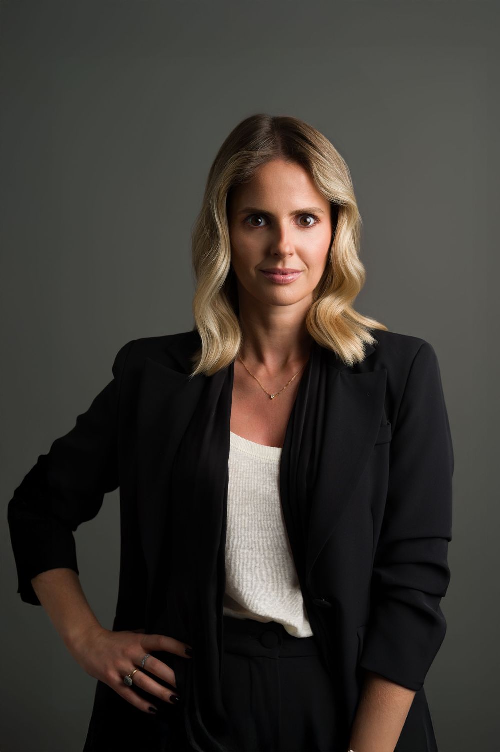 Blonde woman in black blazer with hand on hip, professional corporate headshot portrait.