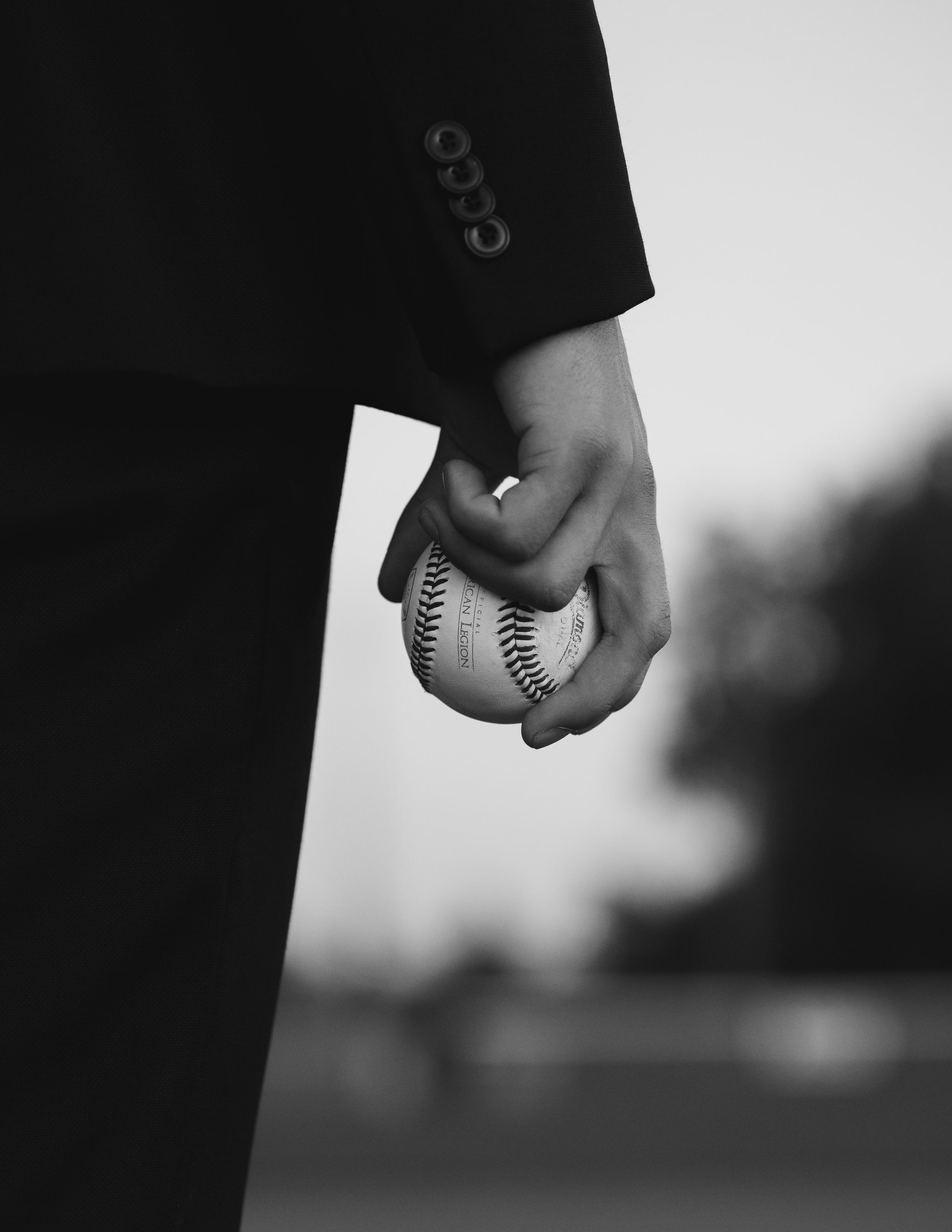 A black and white close-up of a hand holding a baseball against a blurred background.