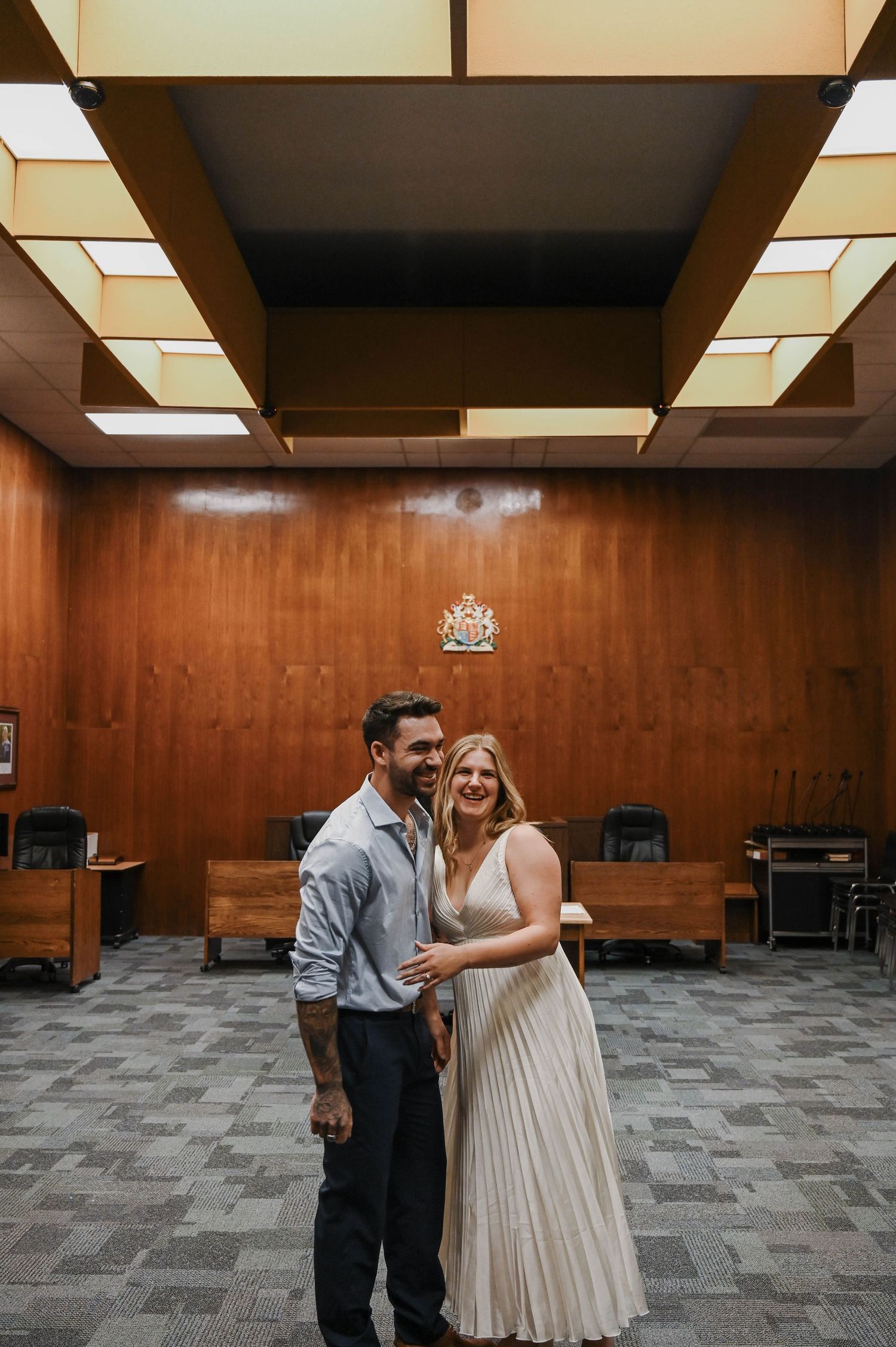 A couple celebrates in a courtroom with geometric ceiling panels and wood-paneled walls during an intimate ceremony.