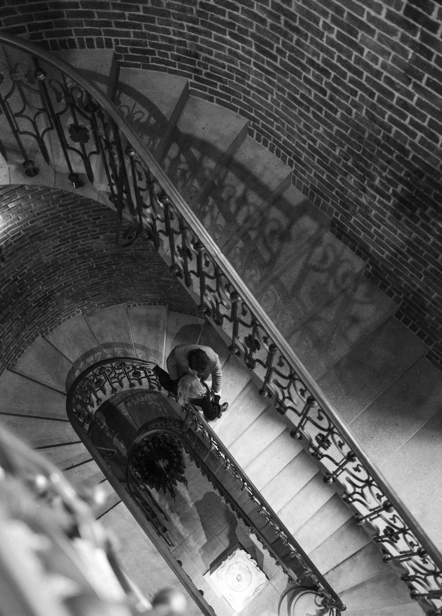 A dramatic black and white photograph of a spiral staircase with ornate iron railings.